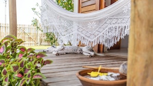 A hammock under a macrame canopy on a wooden deck with a dog lying on it, surrounded by potted plants. - Vilarejo Preá (Cruz)