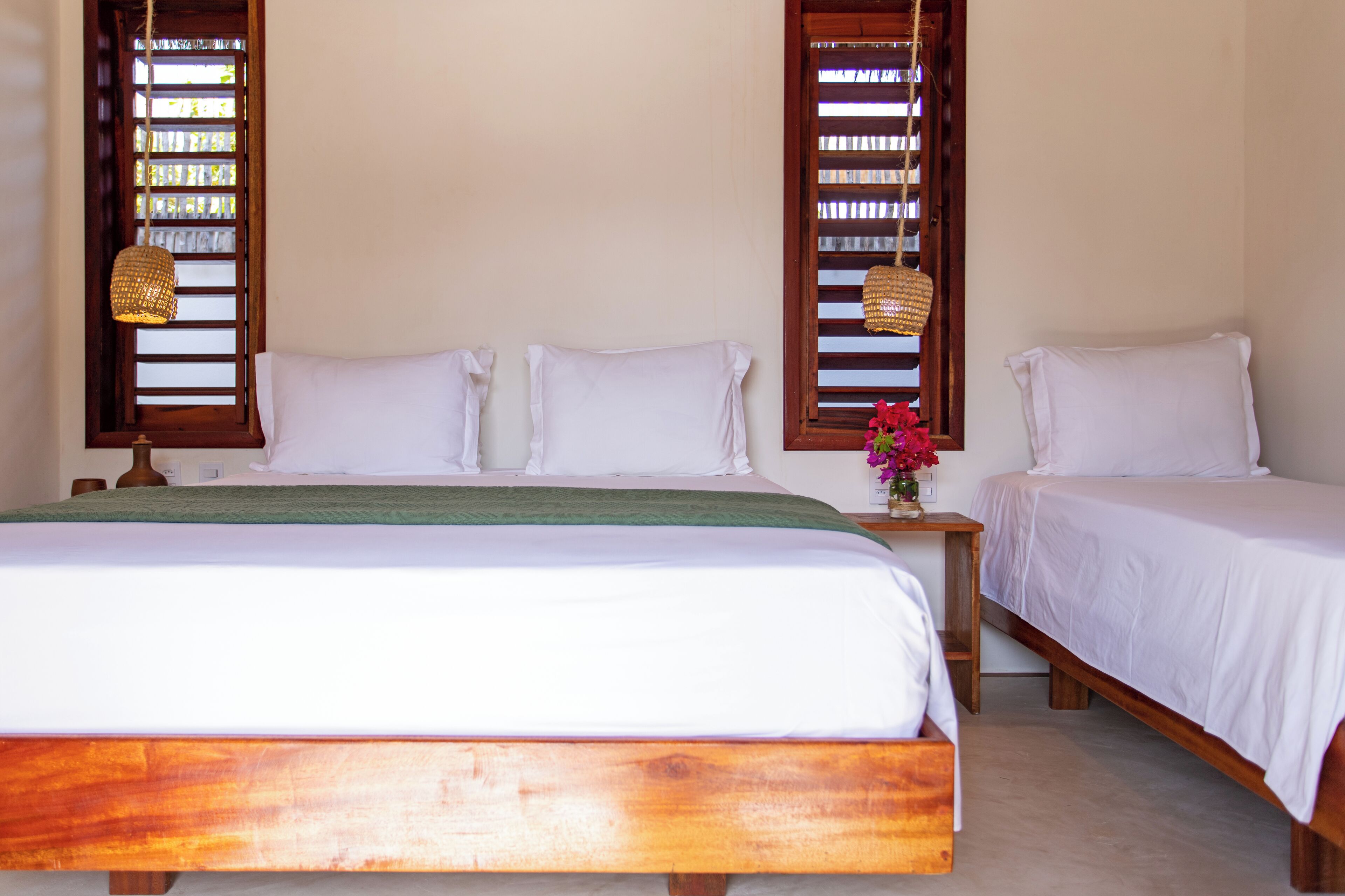 Uma cama de casal com estrutura de madeira, duas mesas de cabeceira e uma mesinha de apoio com um vaso de flores.