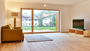 A modern living room with a sofa, a flat-screen TV, and a large sliding glass door leading to a garden.