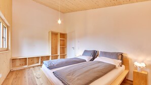 A bedroom with two beds, wooden flooring, a built-in wardrobe, and a bedside table with a lamp.