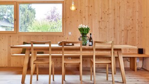 A wooden dining area with a large window, a vase of flowers, and a hanging light fixture.