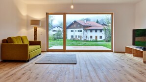 A modern living room with a sofa, a lamp, a TV, and a large window with a view of a house.