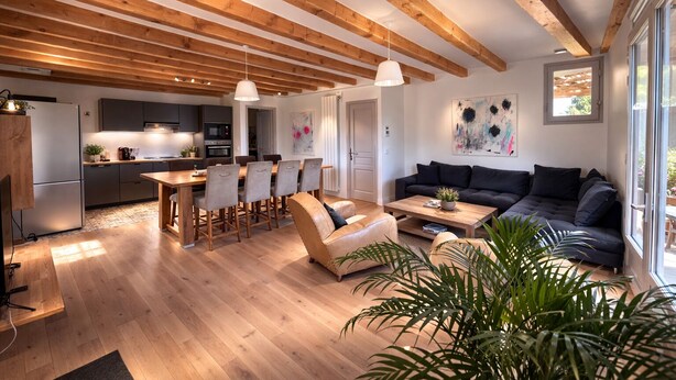 Une cuisine moderne avec des poutres en bois, un coin repas avec une table et des chaises en bois, un canapé de couleur foncée et une table basse.