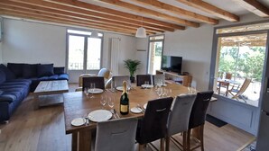 Un vaste espace de vie doté d’un plafond en bois, d’une table à manger pour six personnes, d’un canapé et d’un téléviseur.