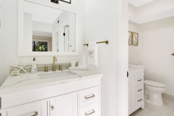 Une salle de bain avec un lavabo, un meuble-lavabo et des toilettes, le tout de couleur blanche.