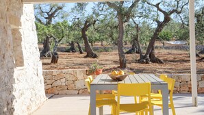 An outdoor patio with a stone wall, a wooden table, and yellow chairs. - TD Trulli Albapetra Pool & Olive Trees (Polignano a Mare)