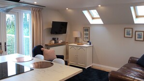 Ein modernes Wohnzimmer mit Essbereich, einem an der Wand montierten Fernseher und einer Decke mit Oberlichtern.