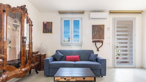 A living room with a blue sofa, a wooden cabinet, and a window with a view. - Villetta La Cornola by BarbarHouse (Taurisano)