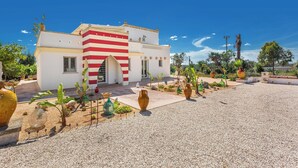 A building with a red and white facade, surrounded by a gravel courtyard with various potted plants and vases. - Villetta La Cornola by BarbarHouse (Taurisano)