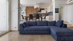 Una sala de estar moderna con un sofá modular, un comedor con mesa y sillas de madera, y una cocina al fondo.