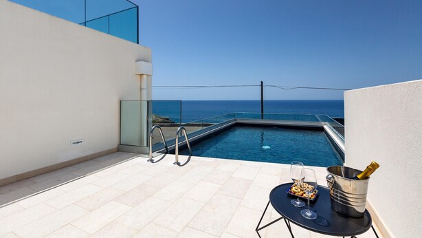 Una piscina en la azotea con vistas despejadas al océano, una mesa con una botella de champán y una copa de vino.