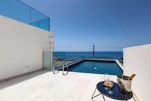 A rooftop pool with a clear view of the ocean, a table with a bottle of champagne, and a glass of wine.