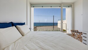 Un dormitorio con una cama grande, un balcón con vista al mar y una silla junto a la ventana.