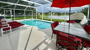 Un área de piscina techada con sillas de reposo rojas, una mesa y una sombrilla.