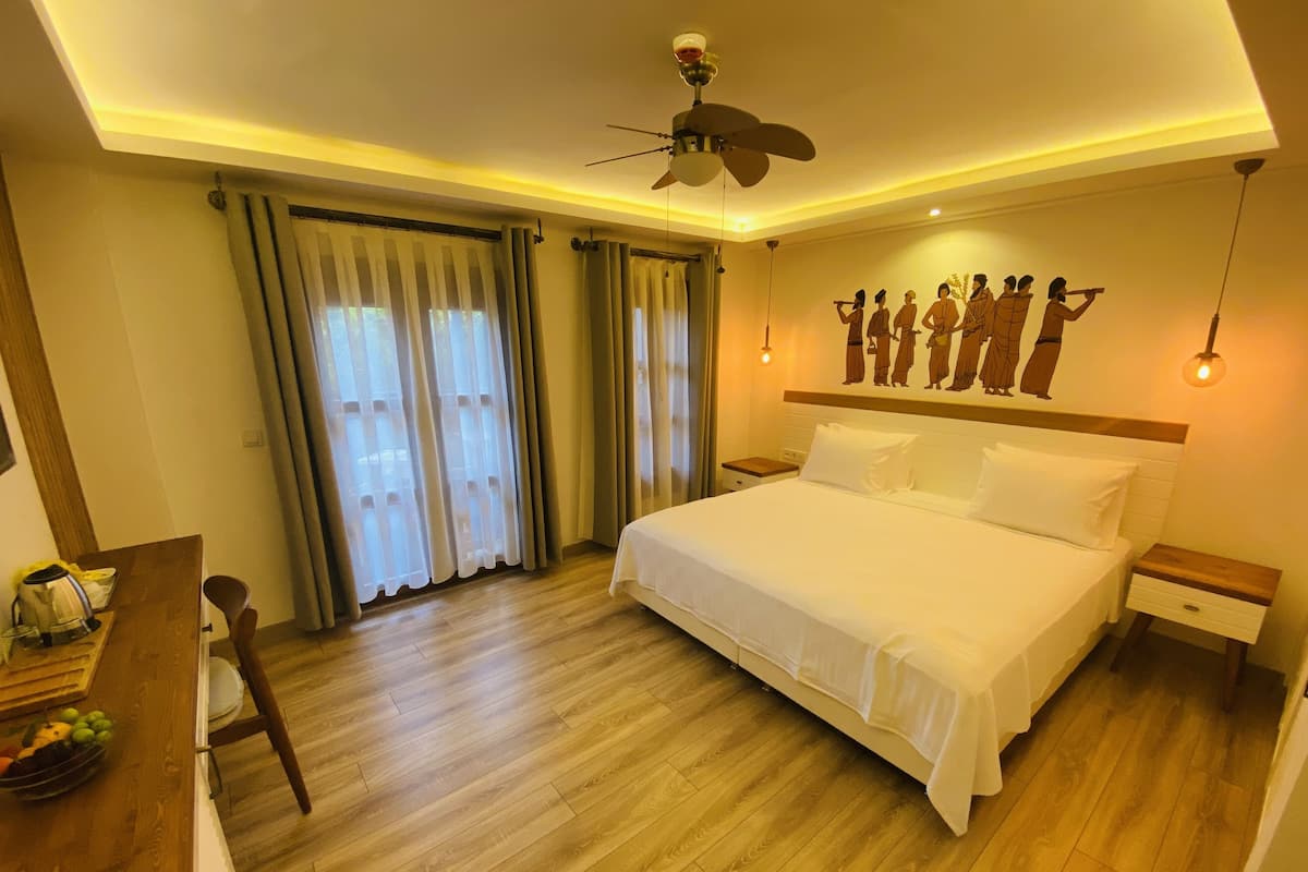 A hotel room with a large bed, wooden flooring, a desk with a chair, and a ceiling fan.