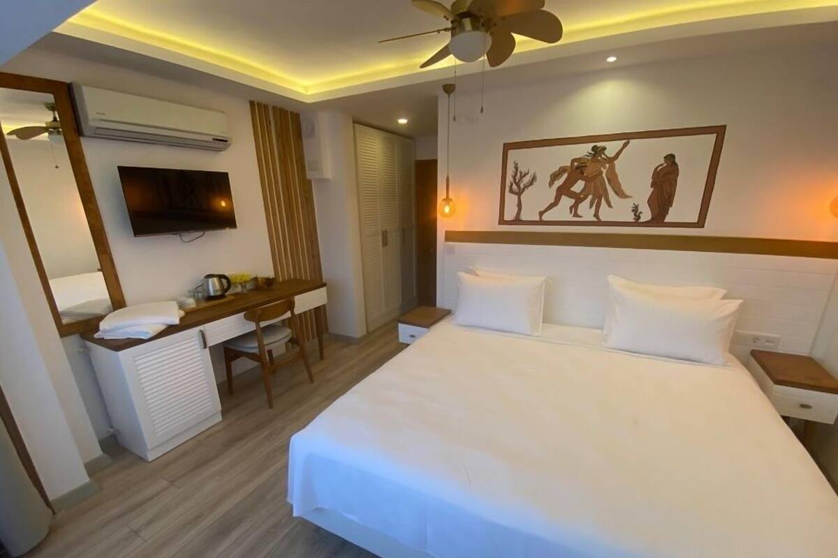 A hotel room with a bed, a desk with a chair, a television, and a painting on the wall.