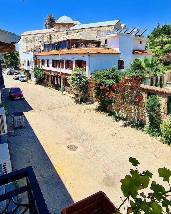 A street view with buildings, a parked car, and a clear blue sky. - In Ephesus Otel and Art Galery (Selçuk)