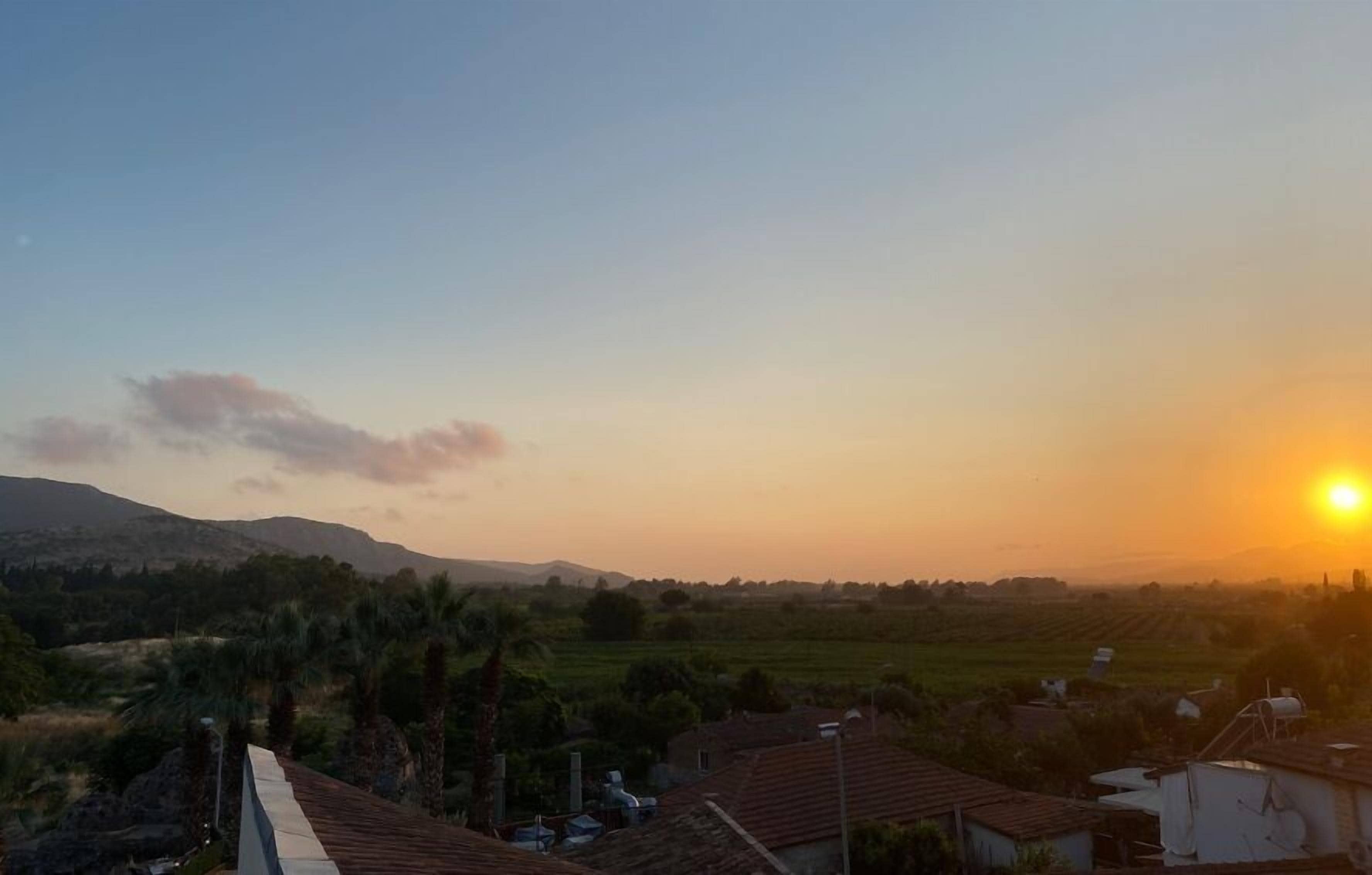 Paisagem rural com pôr do sol, campos e algumas construções espalhadas.