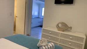 Une chambre à coucher avec un lit, une commode, un téléviseur et une vue sur la cuisine.