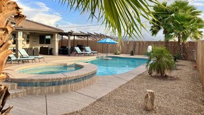A backyard with a swimming pool, lounge chairs, and a barbecue area.