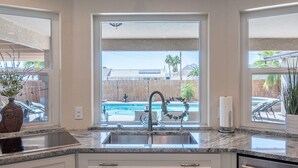 A modern kitchen with a large window, granite countertops, and a view of a swimming pool.