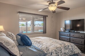A bedroom with a bed, a ceiling fan, a TV, a dresser, and a window with a view of a backyard. - Family Oasis - Pool • Spa • Boat Parking • Sleeps 10 (Lake Havasu City)