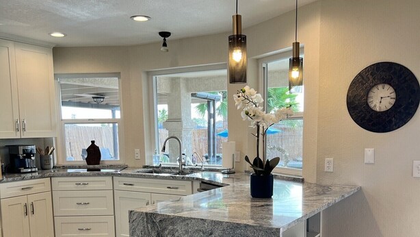 A modern kitchen with a large island, wooden flooring, and pendant lighting.