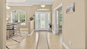 A hallway with a dining area, a chandelier, a door with glass panels, and a potted plant. - Canal Waterfront Home with heated private pool (Palm Coast)