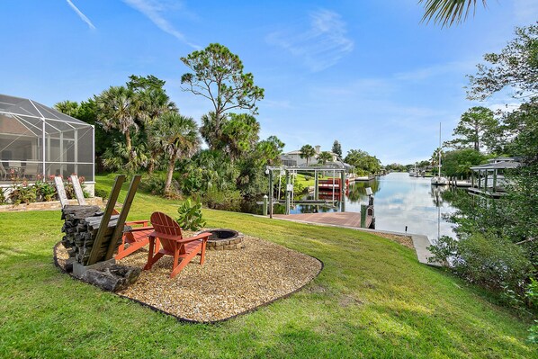 A backyard with a fire pit, outdoor seating, and a view of a lake. - Canal Waterfront Home with heated private pool (Palm Coast)