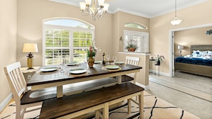 A dining area with a wooden table set for four, a chandelier, and a large window with a view of greenery. - Canal Waterfront Home with heated private pool (Palm Coast)