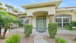 A two-story house with a beige facade, a blue front door, and a curved driveway. - Canal Waterfront Home with heated private pool (Palm Coast)
