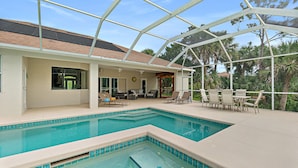 A pool area with a glass enclosure, lounge chairs, and a view of palm trees. - Canal Waterfront Home with heated private pool (Palm Coast)