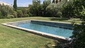 Ein rechteckiger Swimmingpool, umgeben von gepflegtem Rasen und verschiedenen Bäumen.