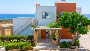 Una casa moderna de dos pisos con un balcón, una escalera que lleva al piso superior y vista al mar.