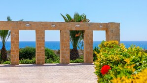 Un arco de piedra con vistas al mar, rodeado de follaje y flores.