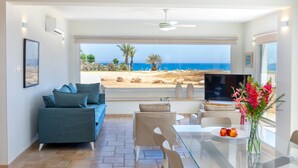 Una sala de estar moderna con un sofá, una mesa de vidrio y vista a la playa.