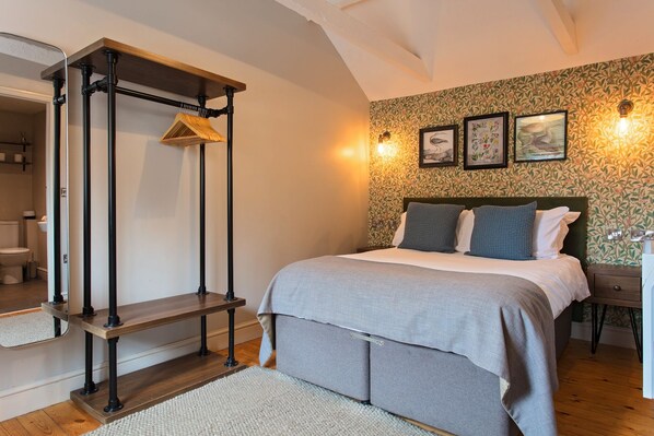 Un dormitorio con cama, un banco de madera, una lámpara de pared y un papel tapiz estampado.