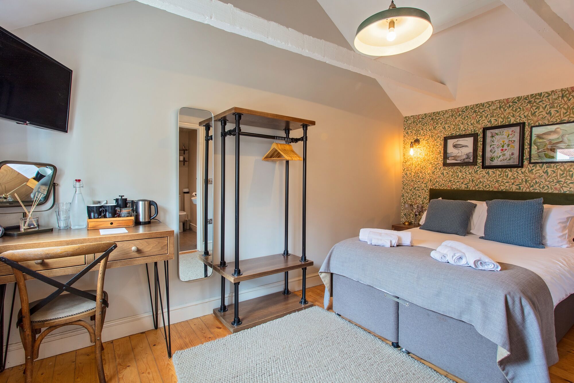 Un dormitorio con cama, mesita de noche, silla, escritorio y espejo.