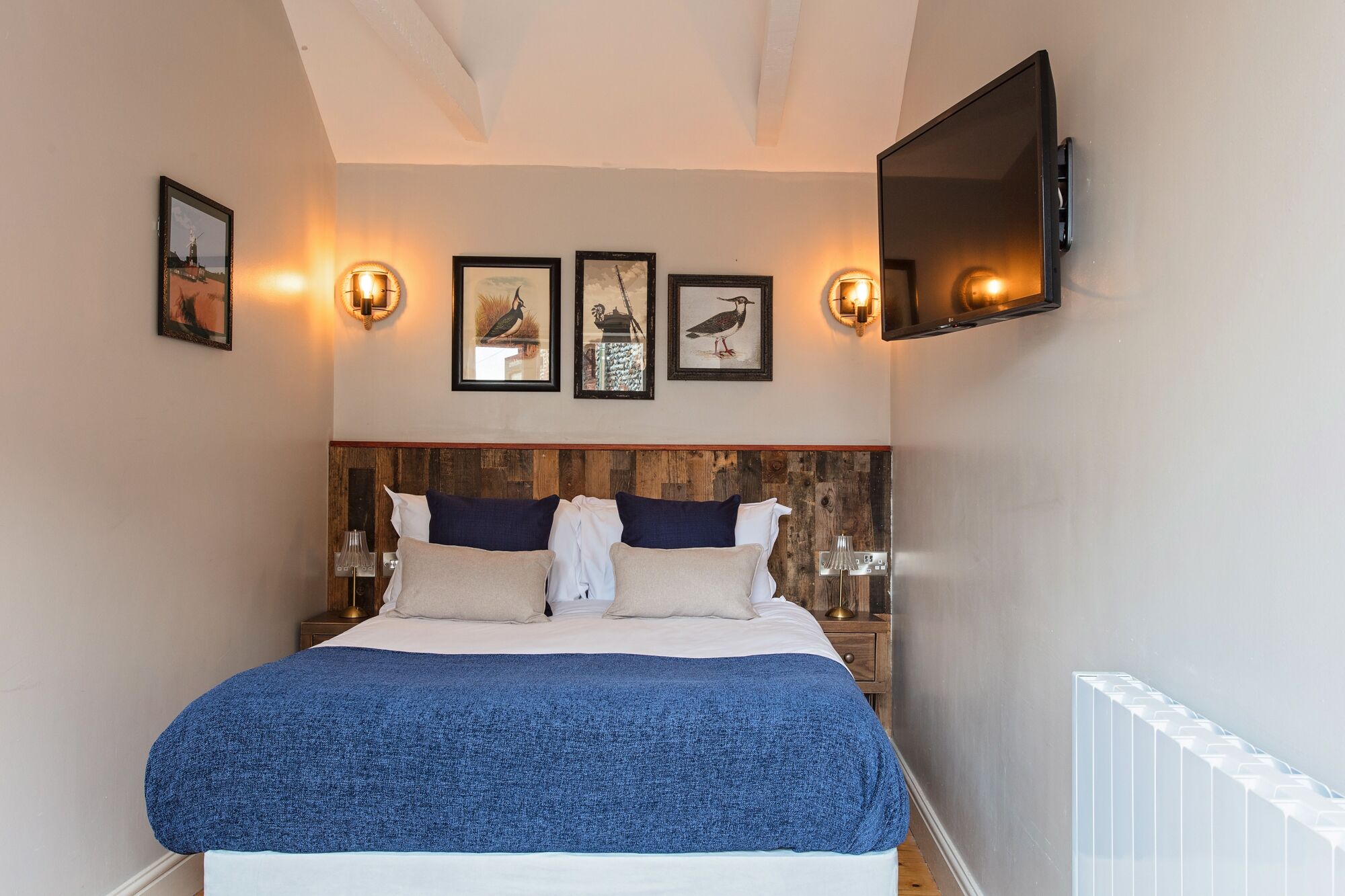 A bedroom with a wooden headboard, a large bed with a blue blanket, and wall-mounted lights.
