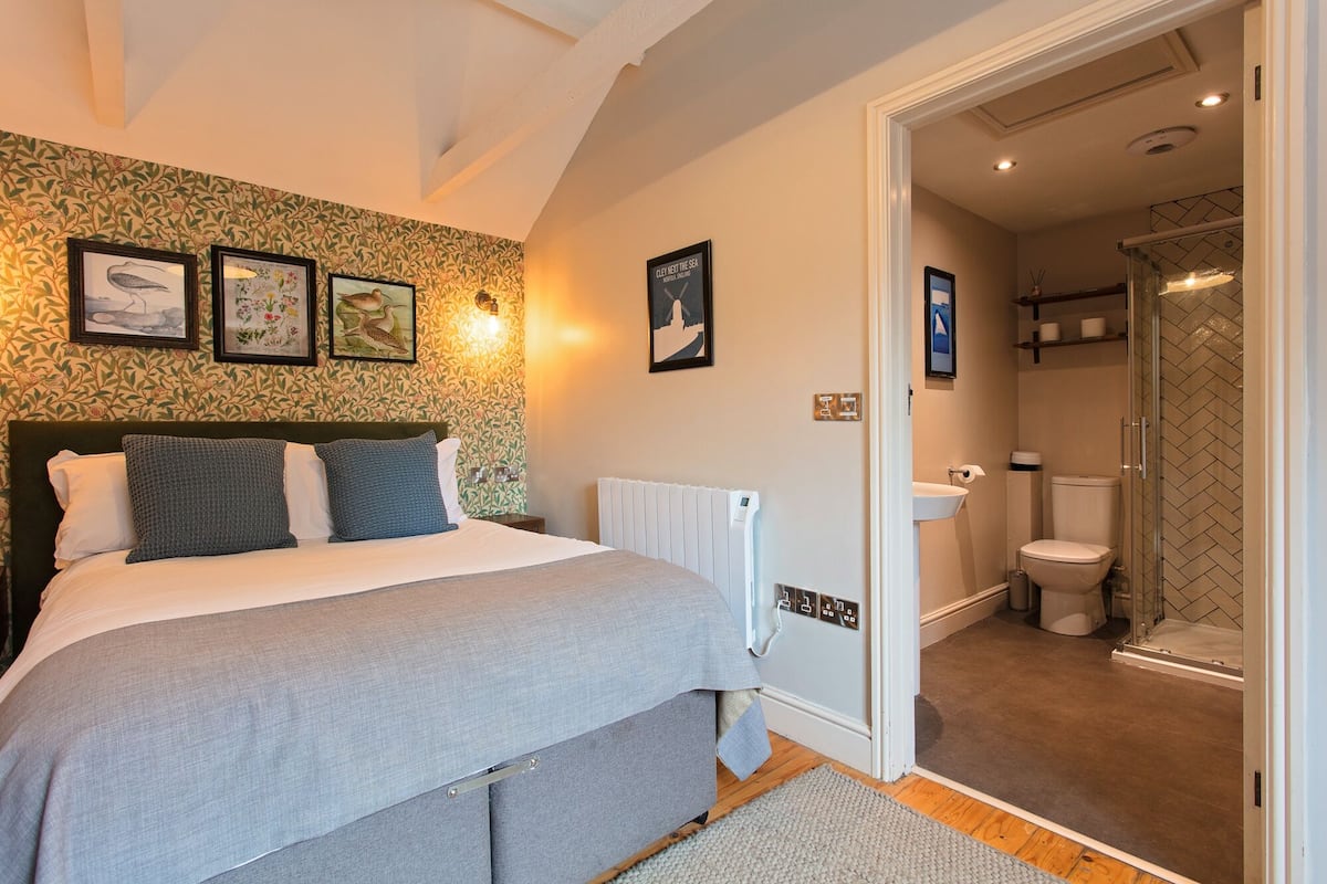 A bedroom with a bed, a radiator, and a bathroom with a toilet and shower.