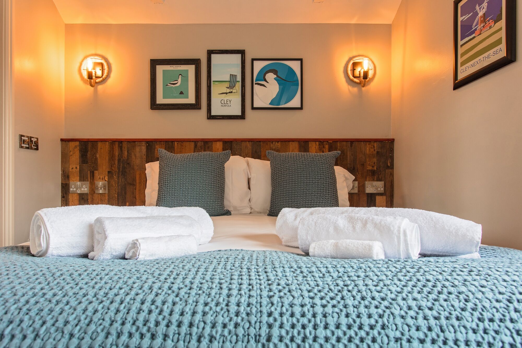 Una habitación de hotel con una cama grande, dos lámparas de pared y tres cuadros en la pared.
