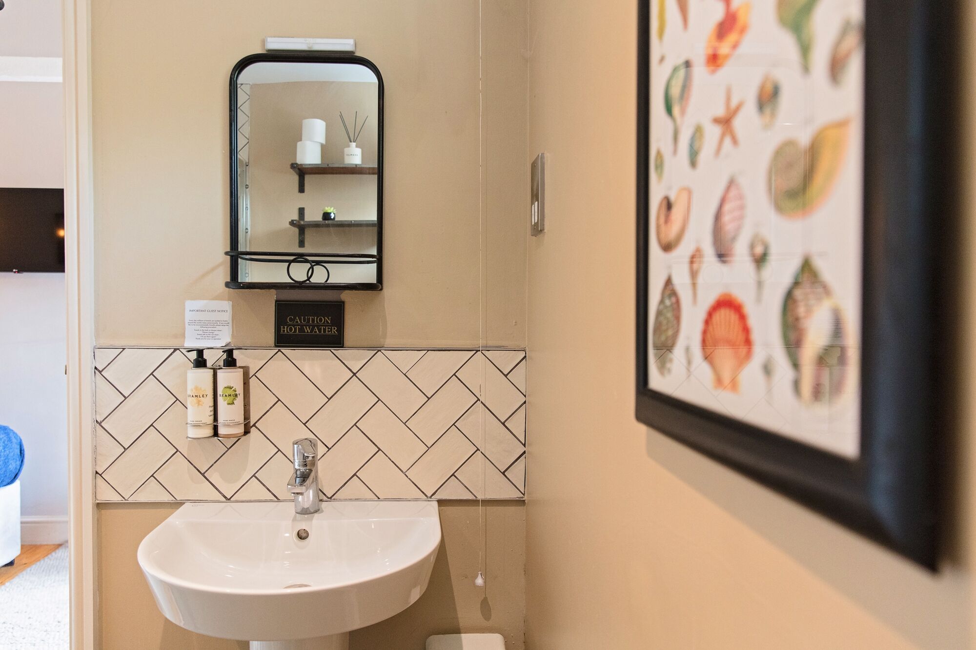 A bathroom with a white sink, a mirror, a caution sign for hot water, and a framed picture of sea creatures.