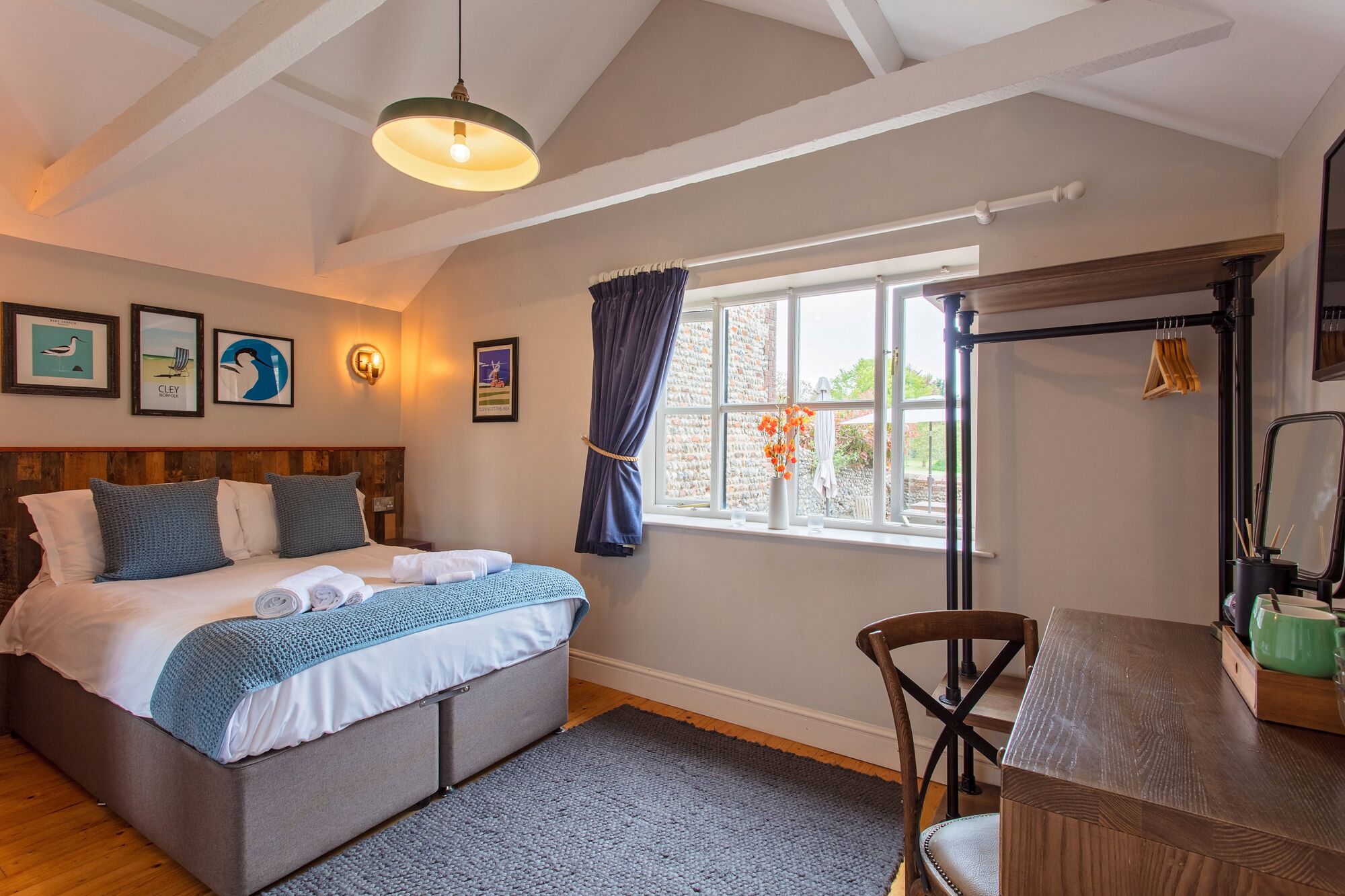 A bedroom with a bed, a desk, a chair, a window with curtains, and a hanging light fixture.