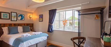 A bedroom with a bed, a desk, a chair, a window with curtains, and a hanging light fixture.