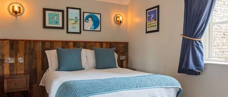 A bedroom with a wooden headboard, a bed with white and blue bedding, a nightstand, and wall-mounted lights.