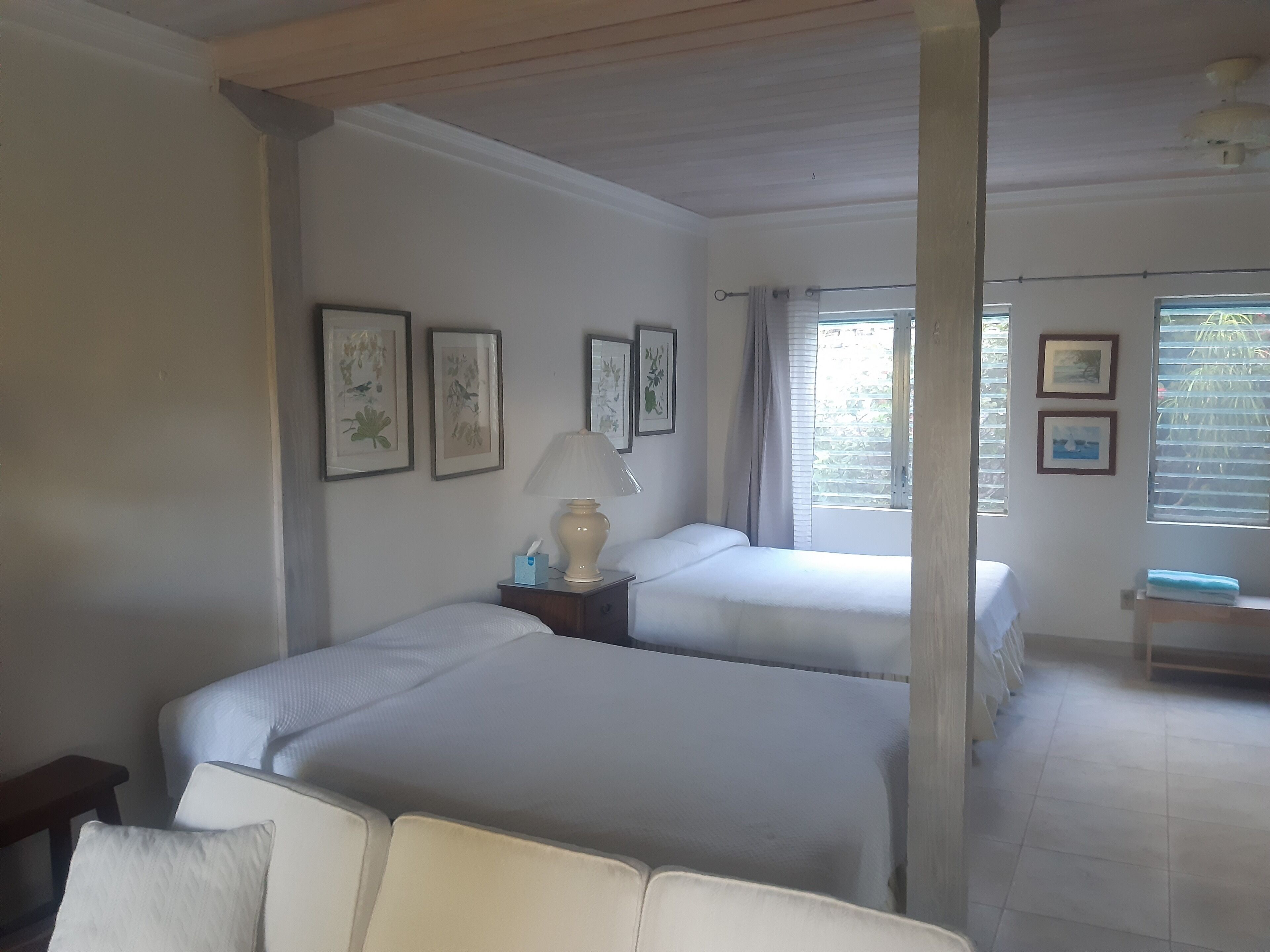 A hotel room with two beds, a bedside table with a lamp, and framed artwork on the wall.