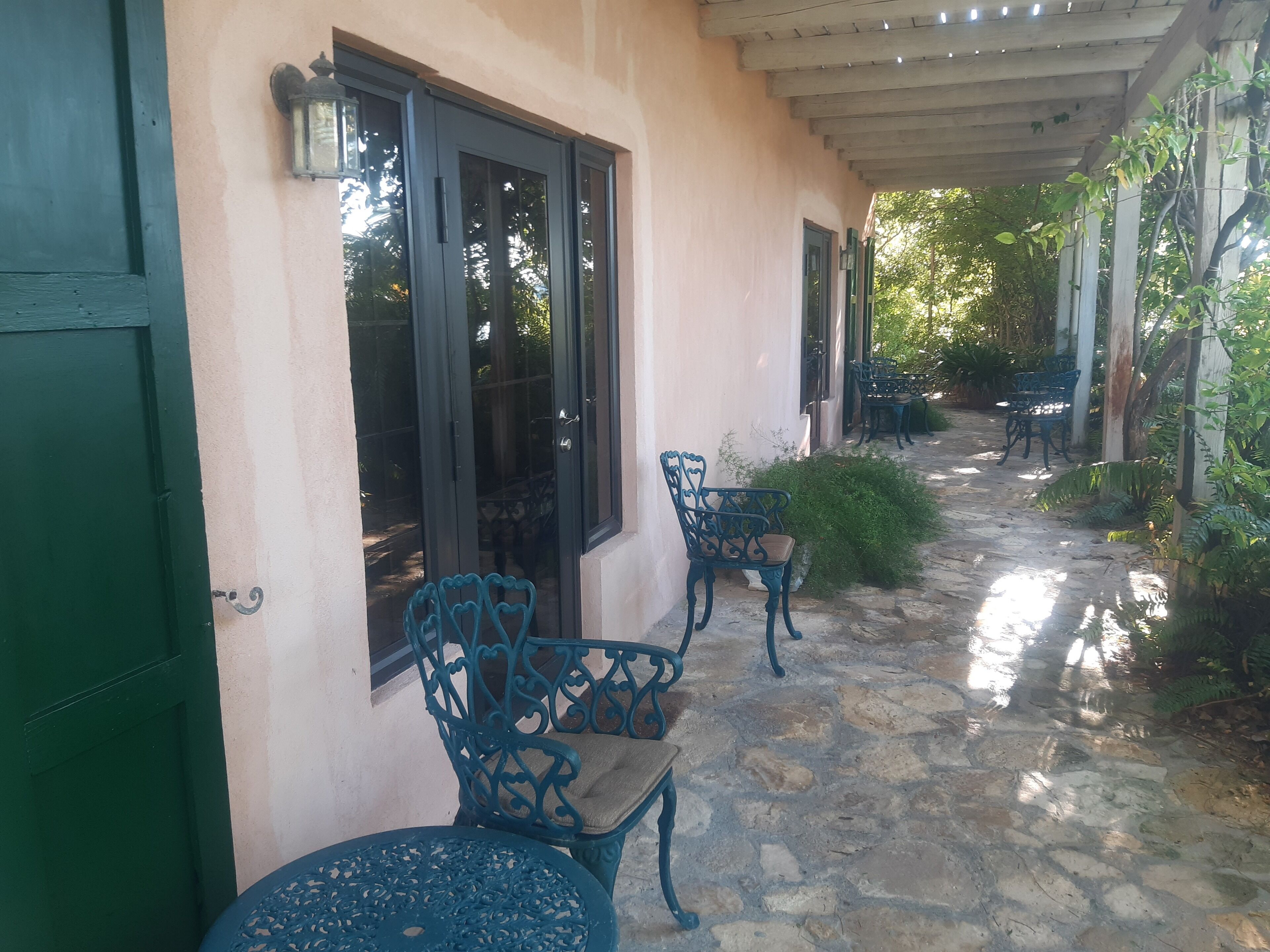A covered outdoor area with stone flooring, green doors, and metal chairs.