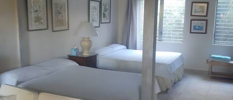 A hotel room with two beds, a sofa, a nightstand with a lamp, and framed pictures on the wall.