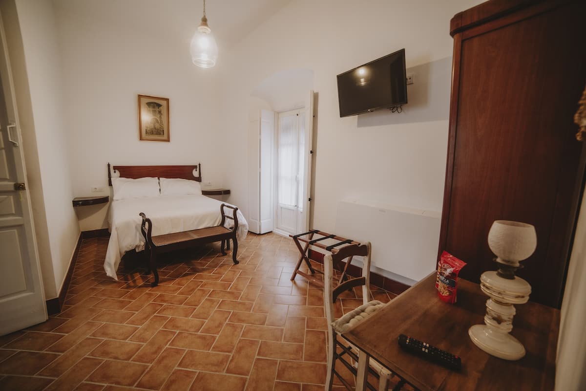 A bedroom with a bed, a chair, a table, a television, and a door.
