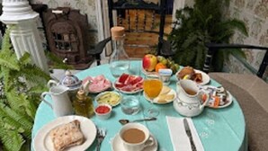 Una mesa redonda con mantel azul claro, dispuesta con alimentos para el desayuno como pan, huevos, fruta y bebidas.